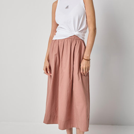 Woman wearing a white sleeveless top and pink skirt on a plain background