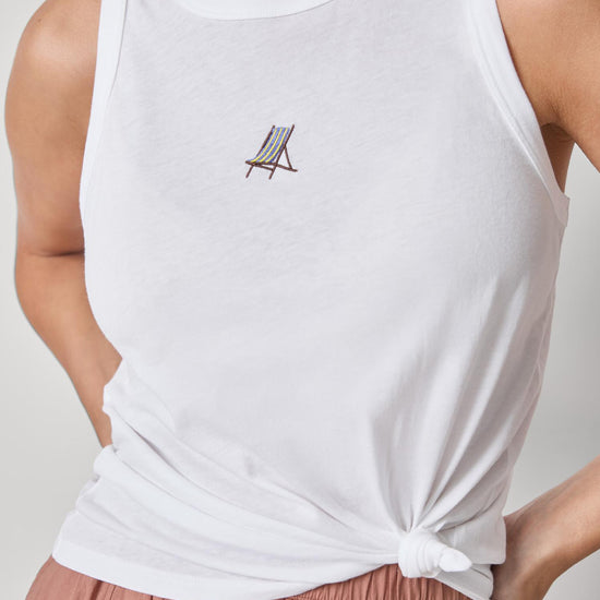 White tank top with a small logo worn by a person on a plain background