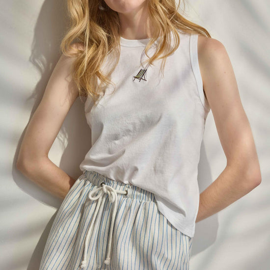 Woman wearing a white sleeveless top and striped shorts against a neutral background