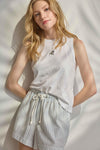 Woman wearing a white sleeveless top and striped shorts against a neutral background