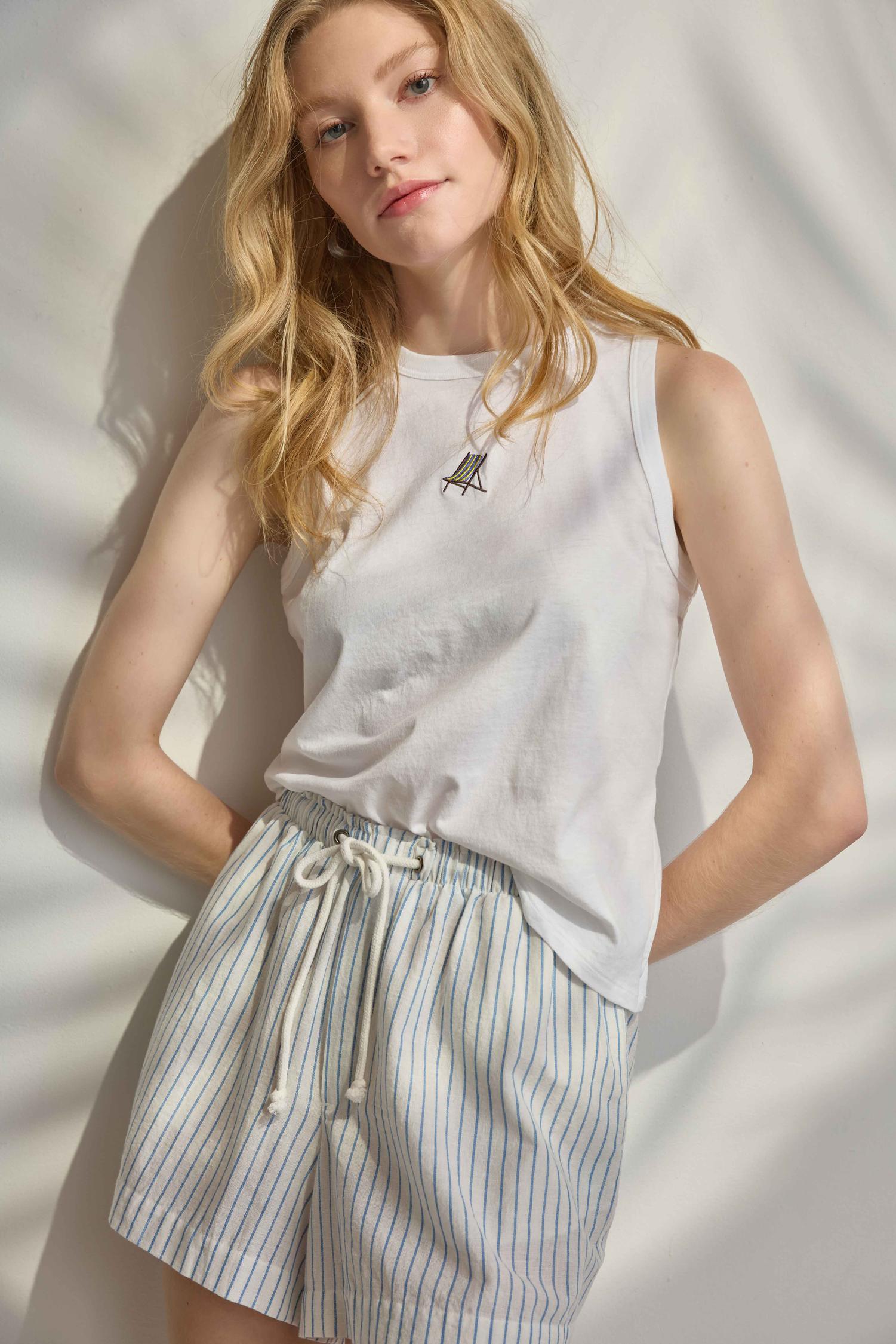 Woman wearing a white sleeveless top and striped shorts against a neutral background