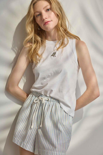 Woman wearing a white sleeveless top and striped shorts against a neutral background