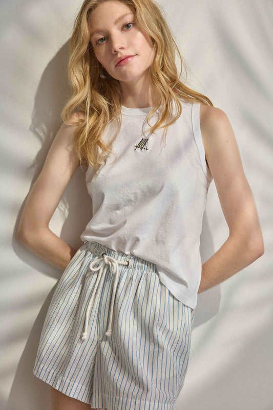 Woman wearing a white sleeveless top and striped shorts against a neutral background