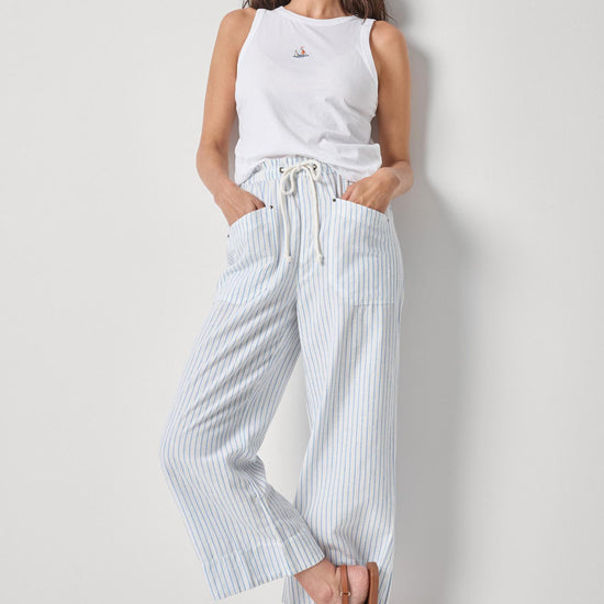 Woman wearing a white sleeveless top and striped pants against a plain background